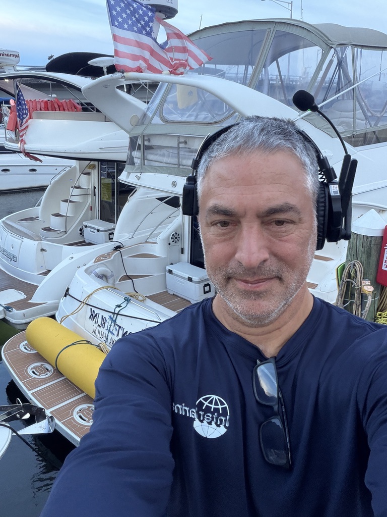 Captain Javier wearing a communication headset beside Don't Blink and Crescendo at the marina